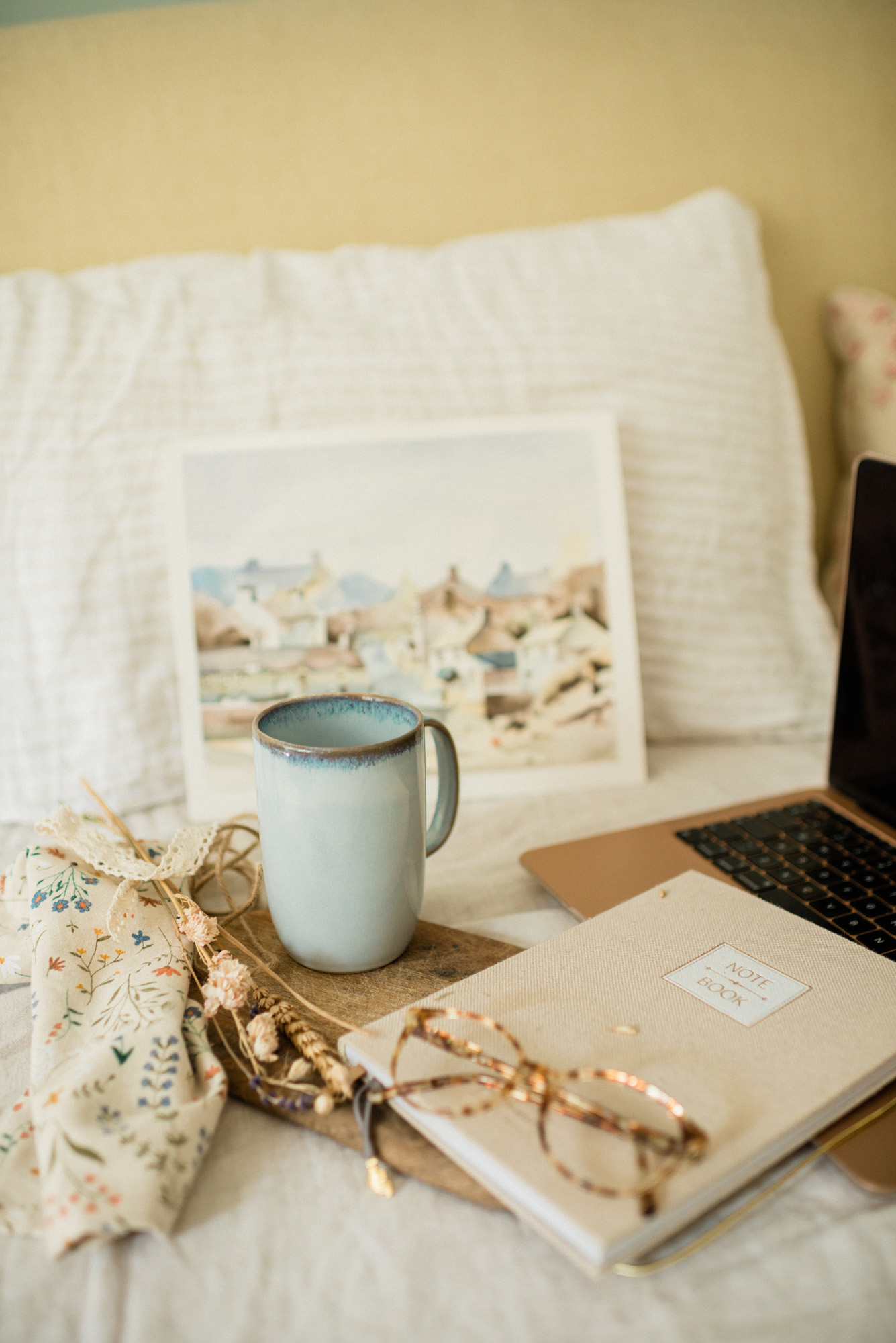 Notitieboek met pen, mok koffie en bril op een bed tijdens het herschrijven van een manuscript